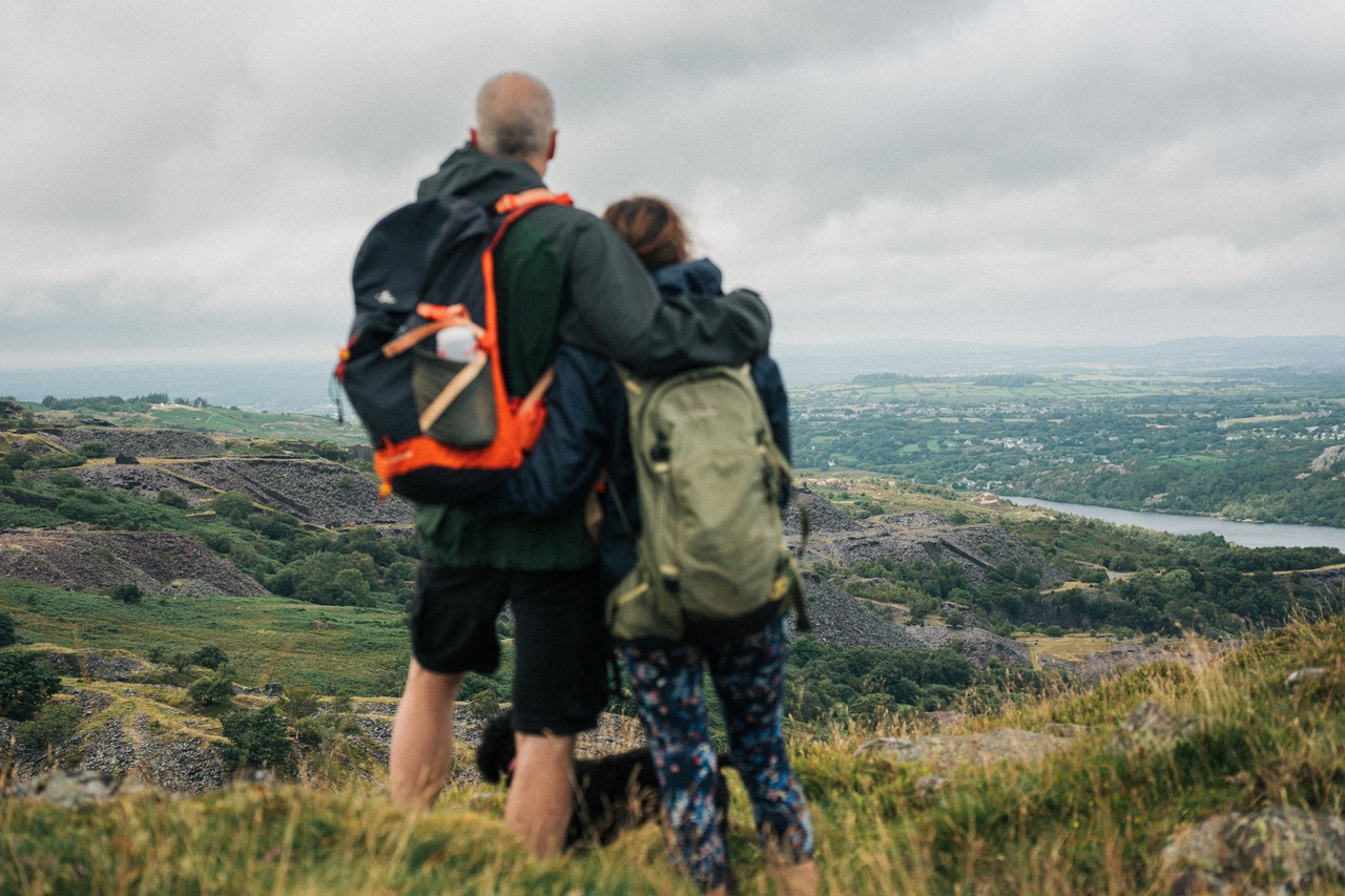 image of a man with his arms around a woman whilst they enjoy the view from a hill top.