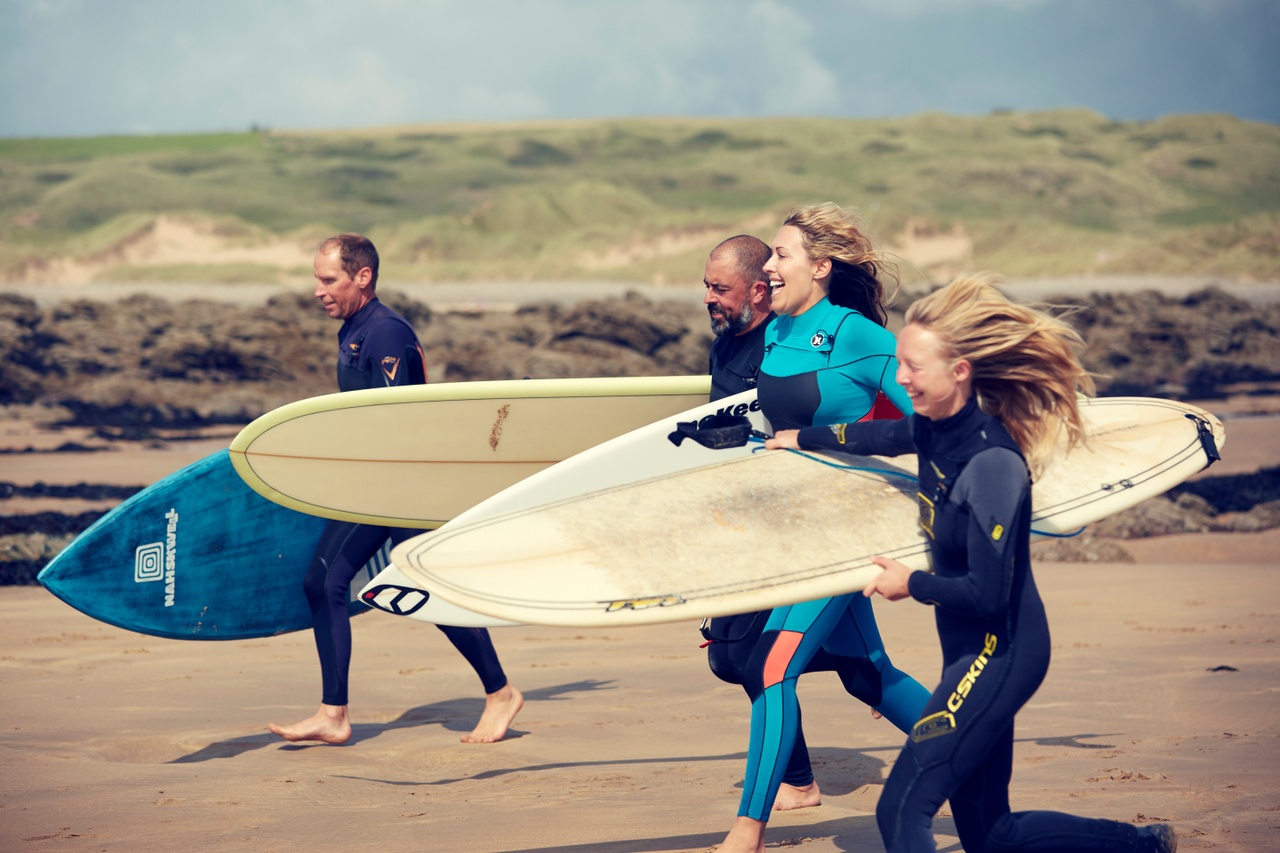 Group of people in wetsuits running on the beach with surfboards.