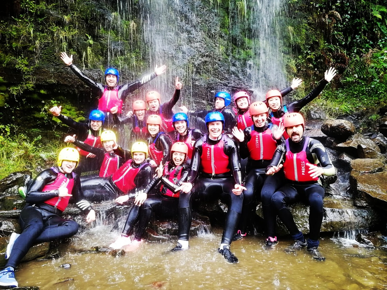 Large group of people celebrating Hwyl in safety gear under waterfalls on a team building event