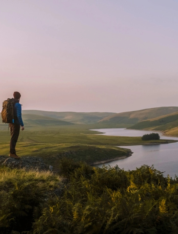 Man with rucksack looking across hills to the water of Craig Goch in Elan Valley