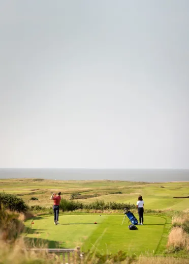 Man and woman playing golf at the Royal Porthcawl Golf Club, South Wales
