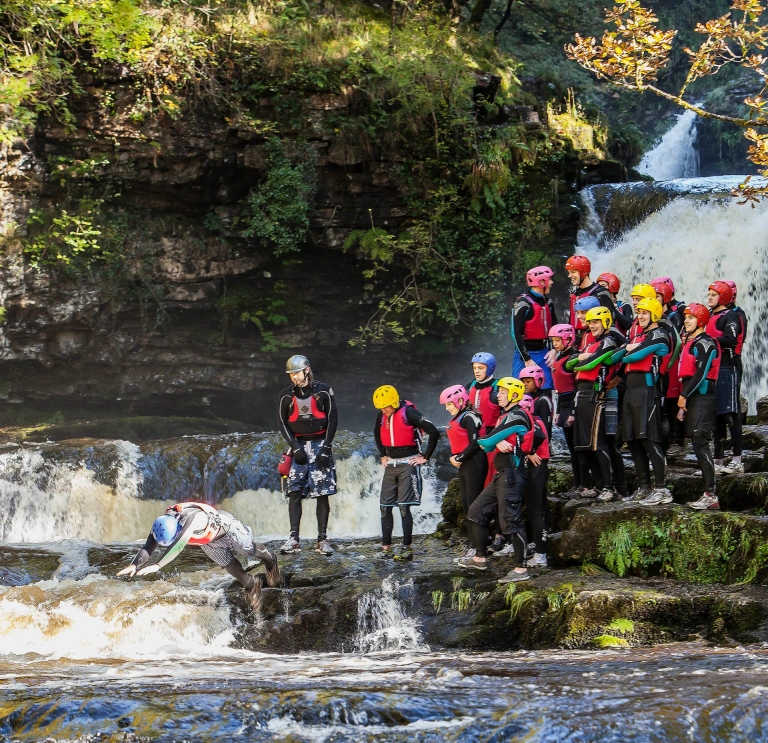 A group of people in safety gear diving near a waterfall.