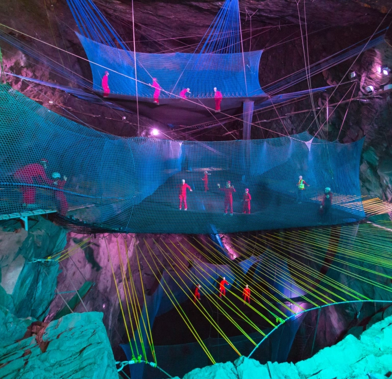 Group of people in safety gear bouncing on nets in an underground cave.