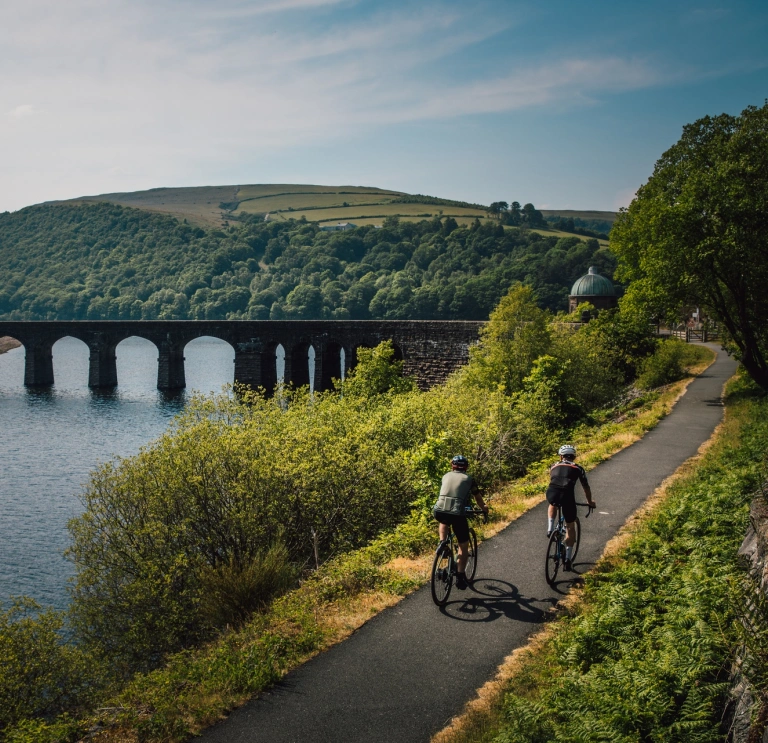 Two cyclists heading toward a footbridge crossing a vast lake.