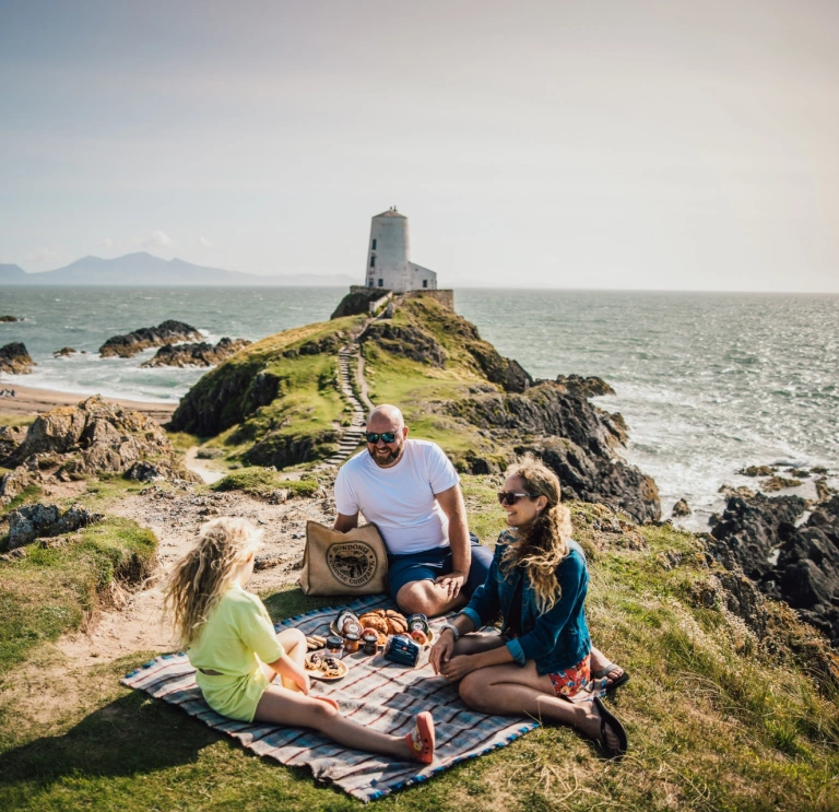 Family having a picnic on a coastal hill near a lighthouse. 