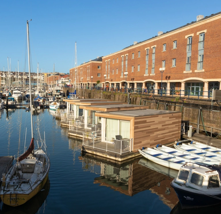 Looking across Milford Haven marina waterfront to boats, floating glamping pods and buildings