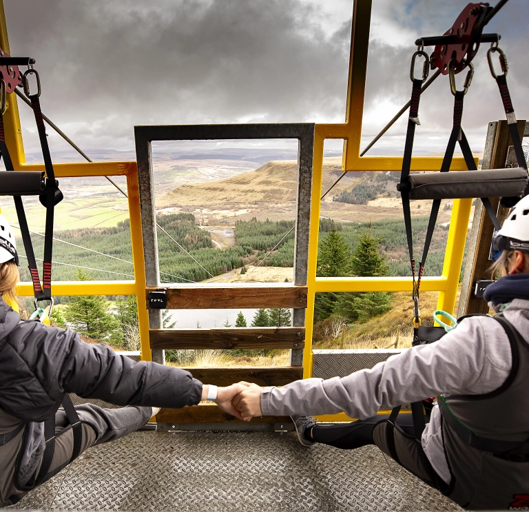Two people sitting on a platform about to do a zipline.