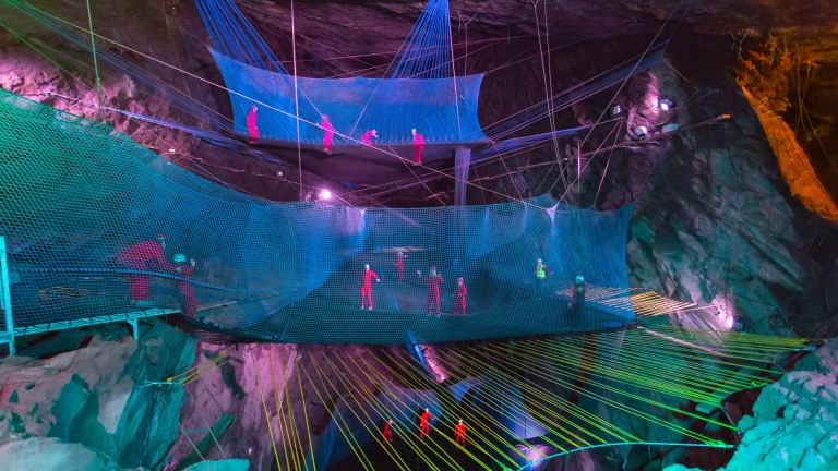 Group of people in safety gear bouncing on nets in an underground cave.