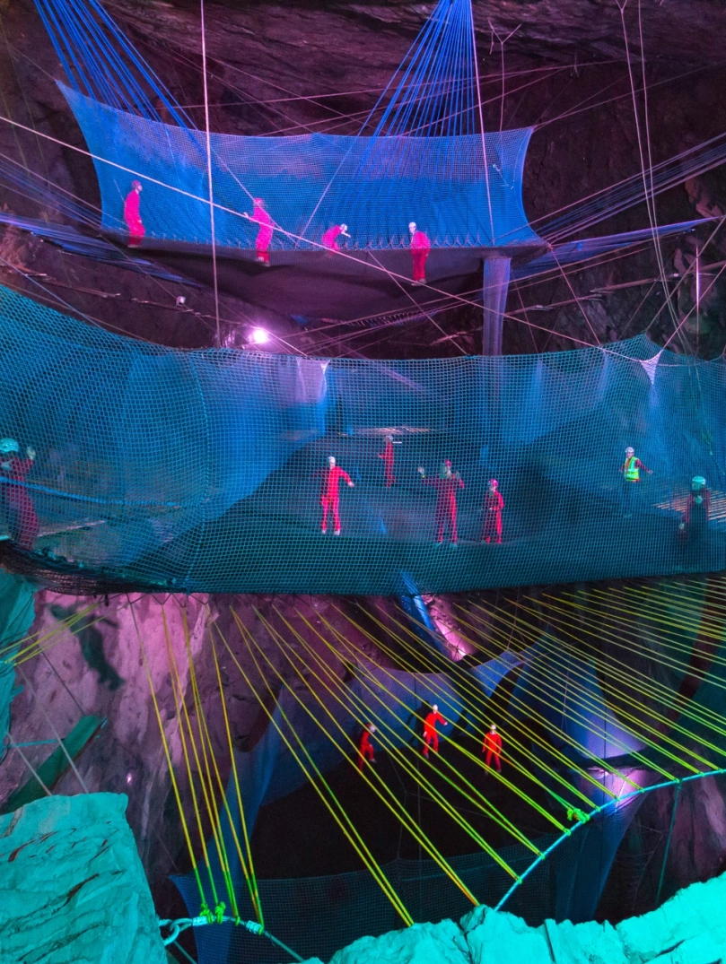 Group of people in safety gear bouncing on nets in an underground cave.