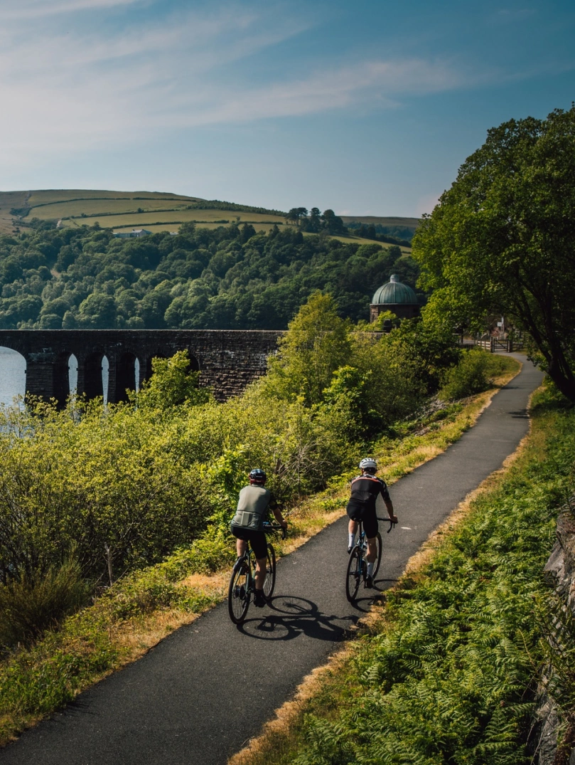 Two cyclists heading toward a footbridge crossing a vast lake.