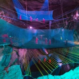 Group of people in safety gear bouncing on nets in an underground cave.