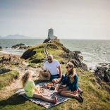 Family having a picnic on a coastal hill near a lighthouse.