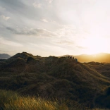 A group of people walking over sand dunes with the sun setting in the background